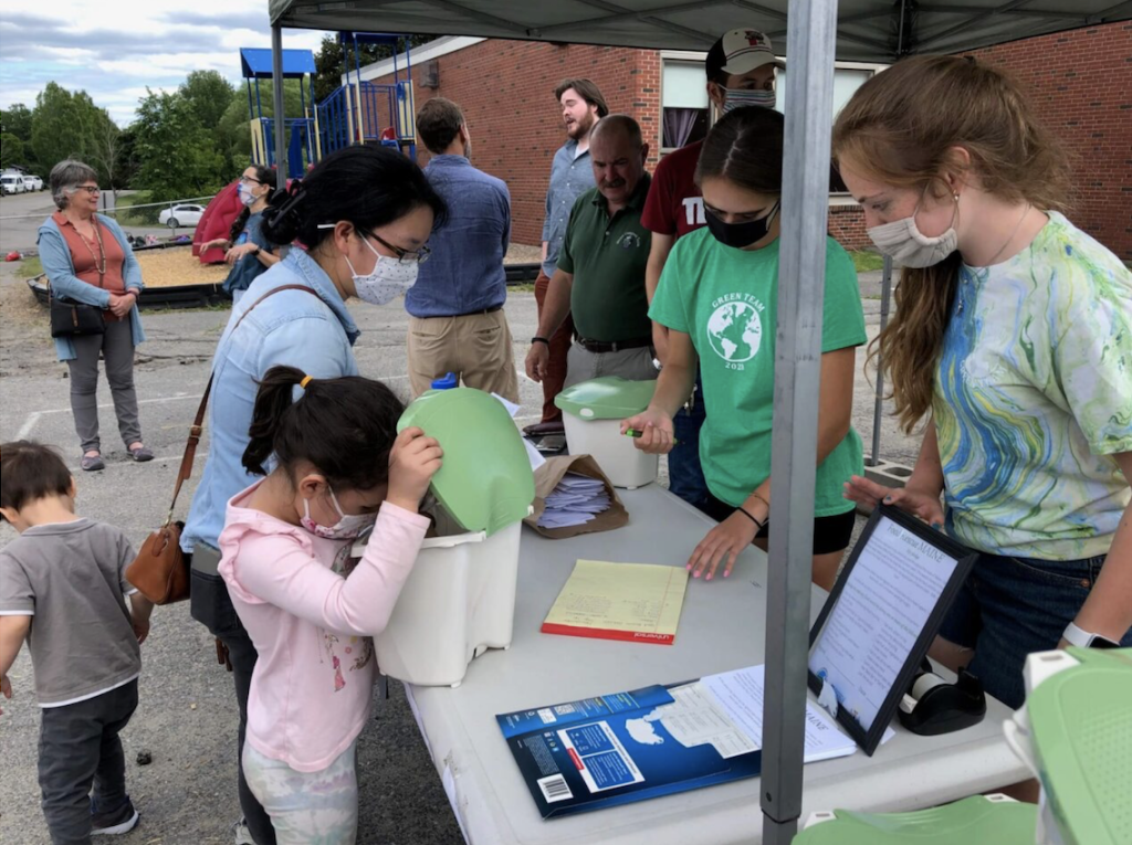 A woman signing something while a kid looks at a compost bucket